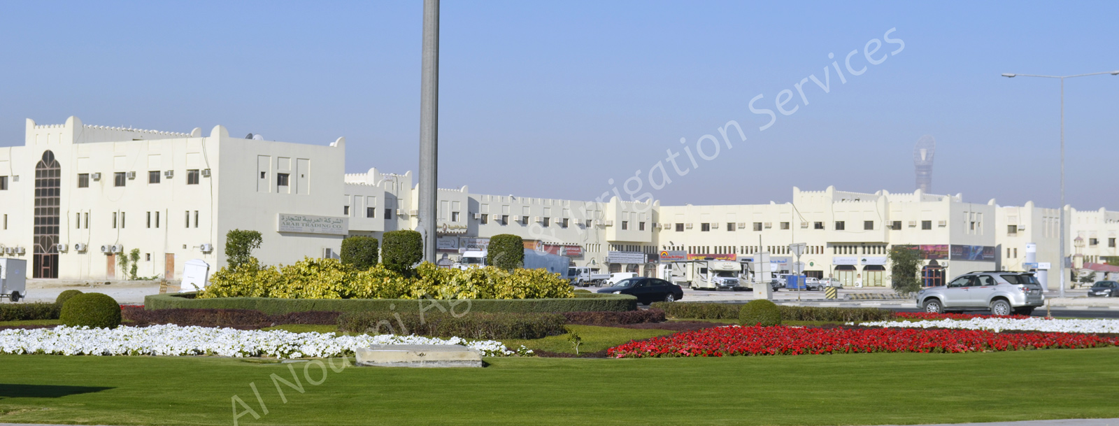Roundabout landscaping with red and white seasonal flower beds, shrubs and lawn in Doha, Qatar