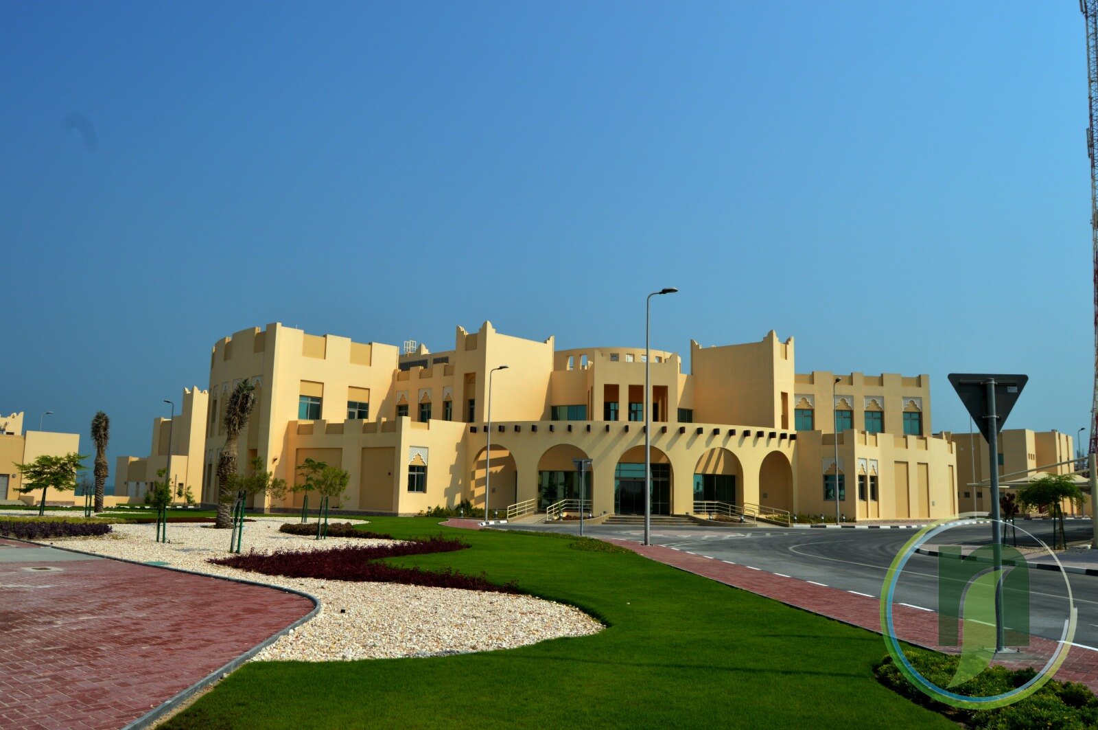 Landscaped lawn, red paving and gravel beds beside a Qatari-style building