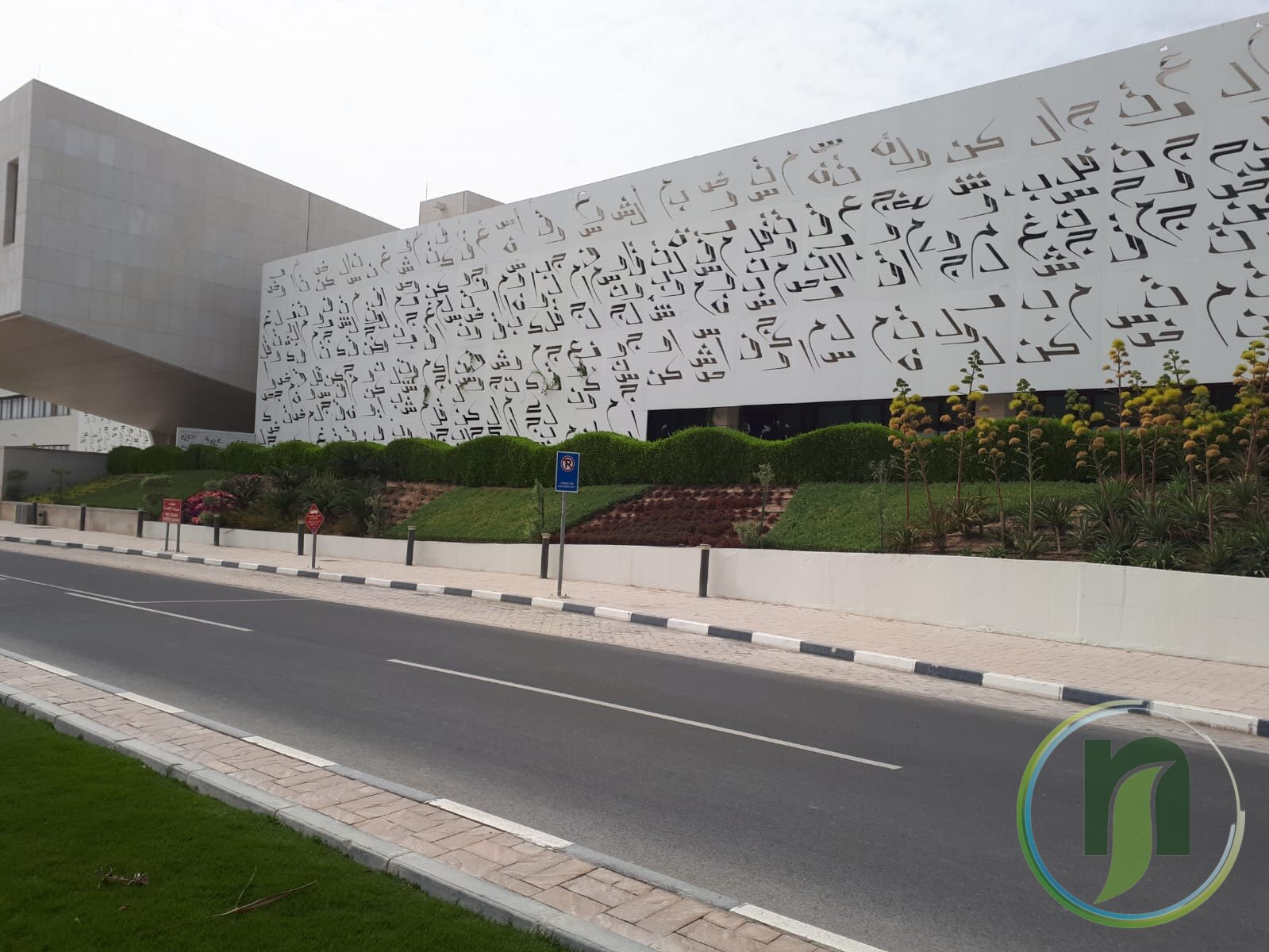 Roadside landscaping with lawn and planting beside a decorative lace-pattern building in Doha